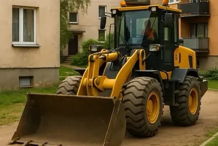 Фронтальный погрузчик работает во дворе жилого дома в ограниченном пространстве